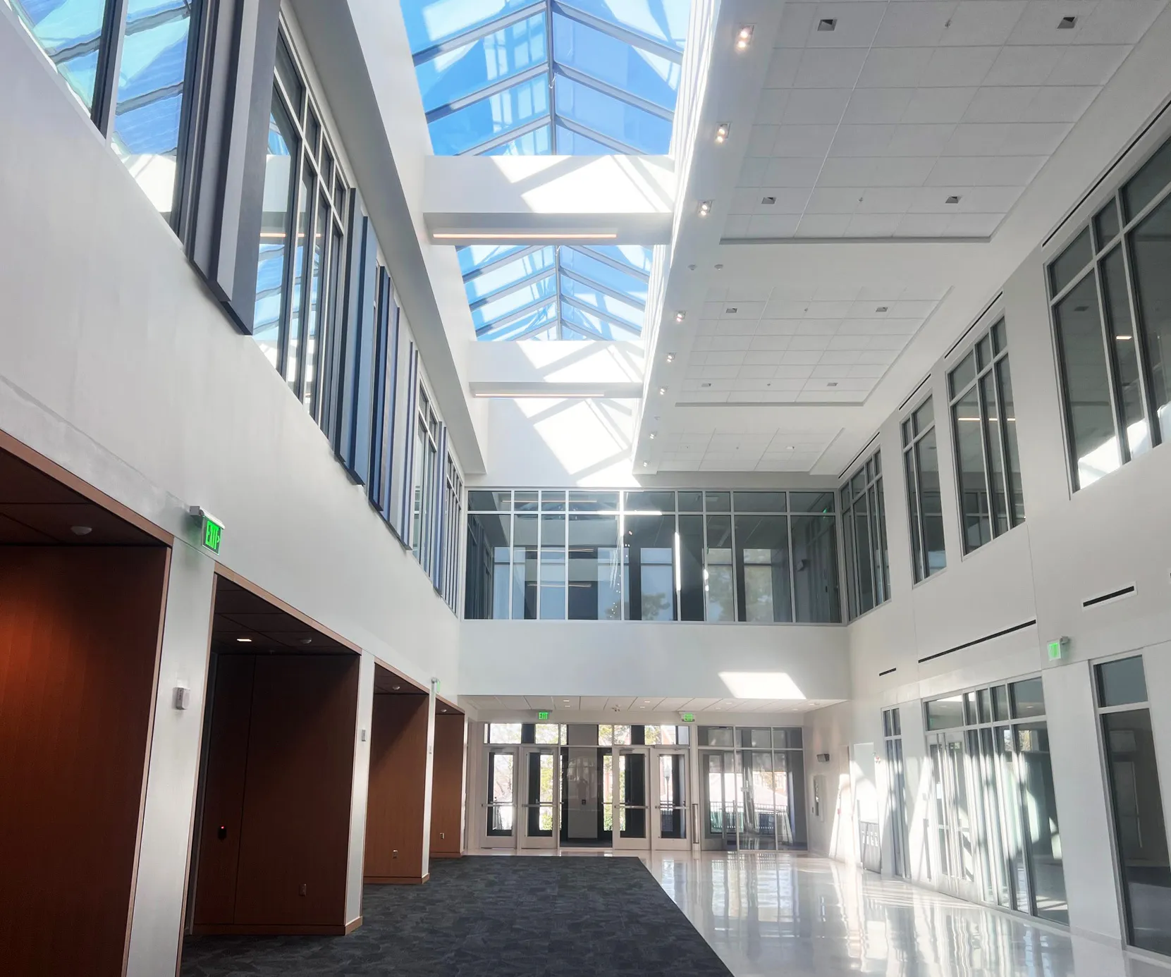 Interior view of a spacious two-story hallway inside the Auburn University College of Education building, featuring tall windows, natural light from a skylight ceiling, and a mix of carpeted and polished floors.