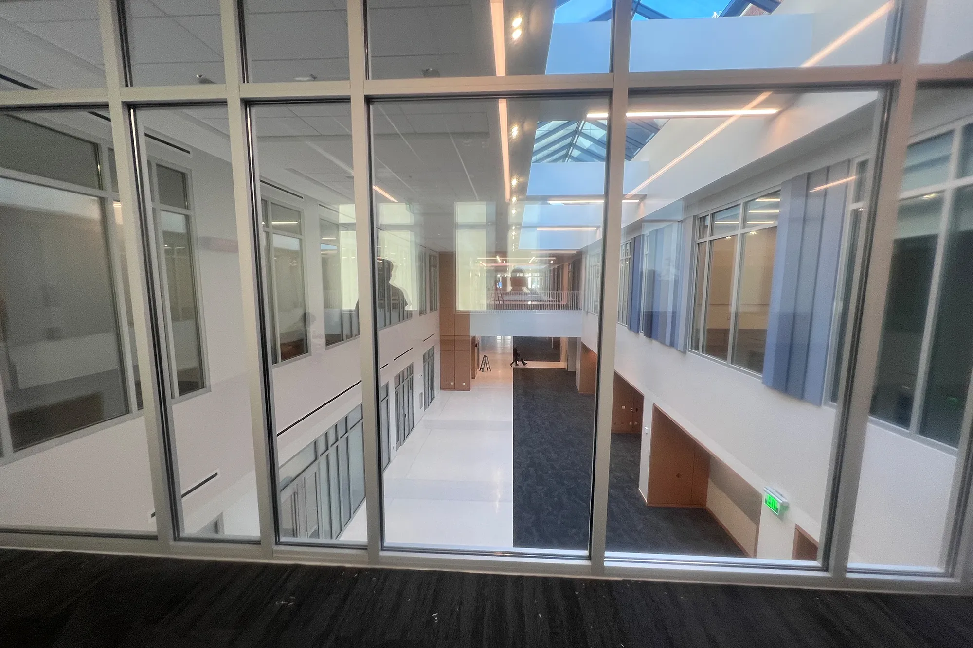 View through large interior windows looking down into a two-story atrium of the Auburn University College of Education building, showing white walls, skylights, and a mix of white tile and dark carpet flooring.