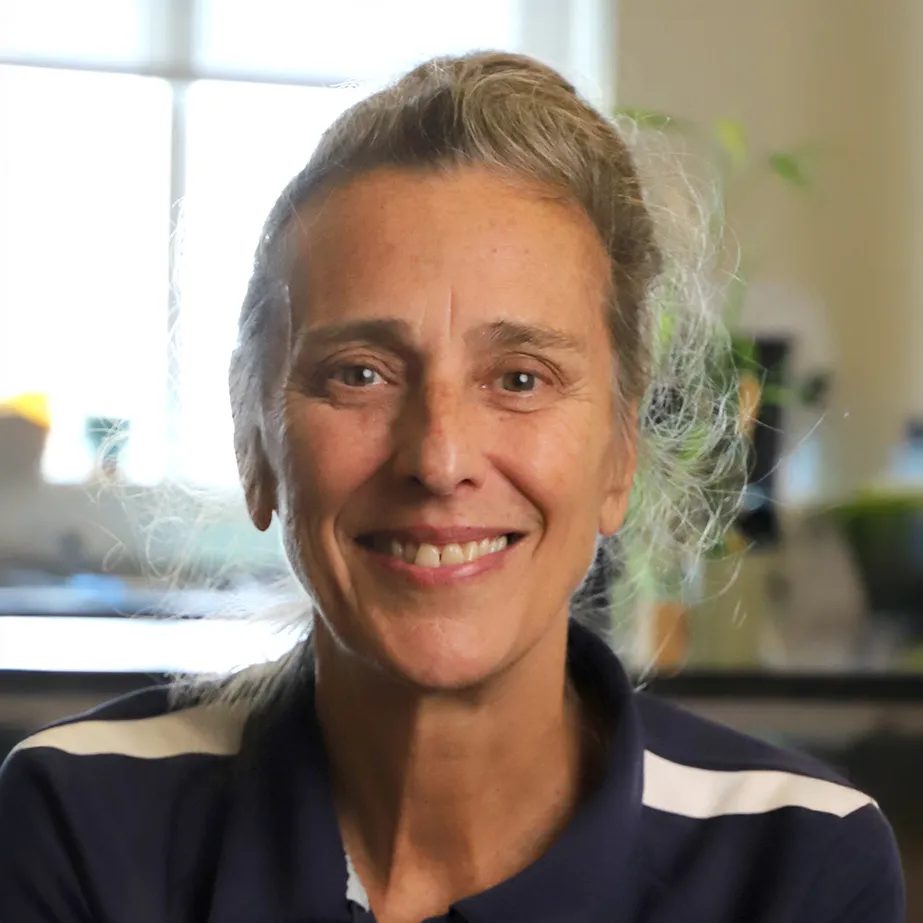 Close-up portrait of a smiling woman wearing an Auburn University polo shirt with a blurred indoor background behind her. Natural light from a window softly illuminates her face.