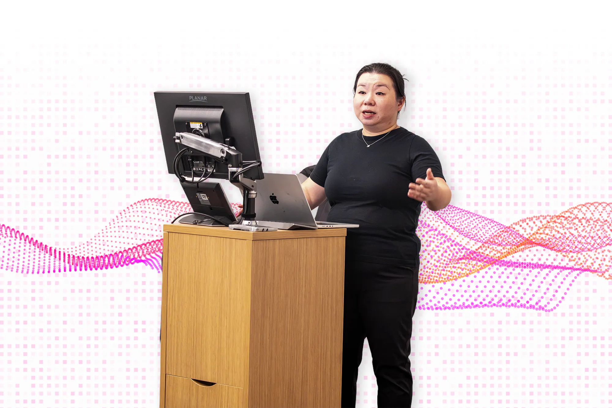 Dr. Mo speaks at a classroom lectern beside a computer monitor and laptop during a presentation on AI.