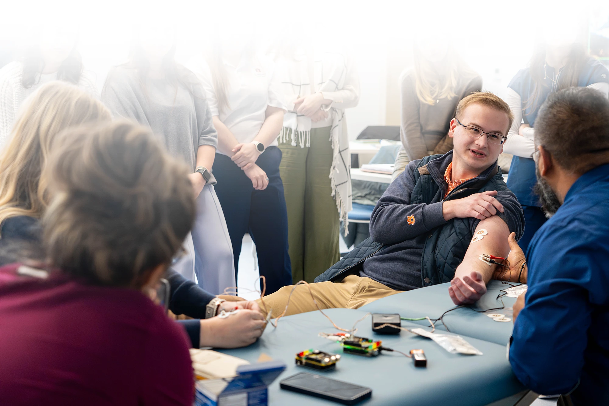 A physical therapy student demonstrates electrode placement on his arm during a hands-on lab exercise as classmates observe.