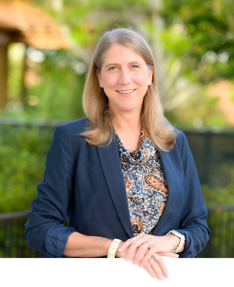 Portrait of Susie Trammell standing outdoors in a navy blazer with a softly blurred campus background.
