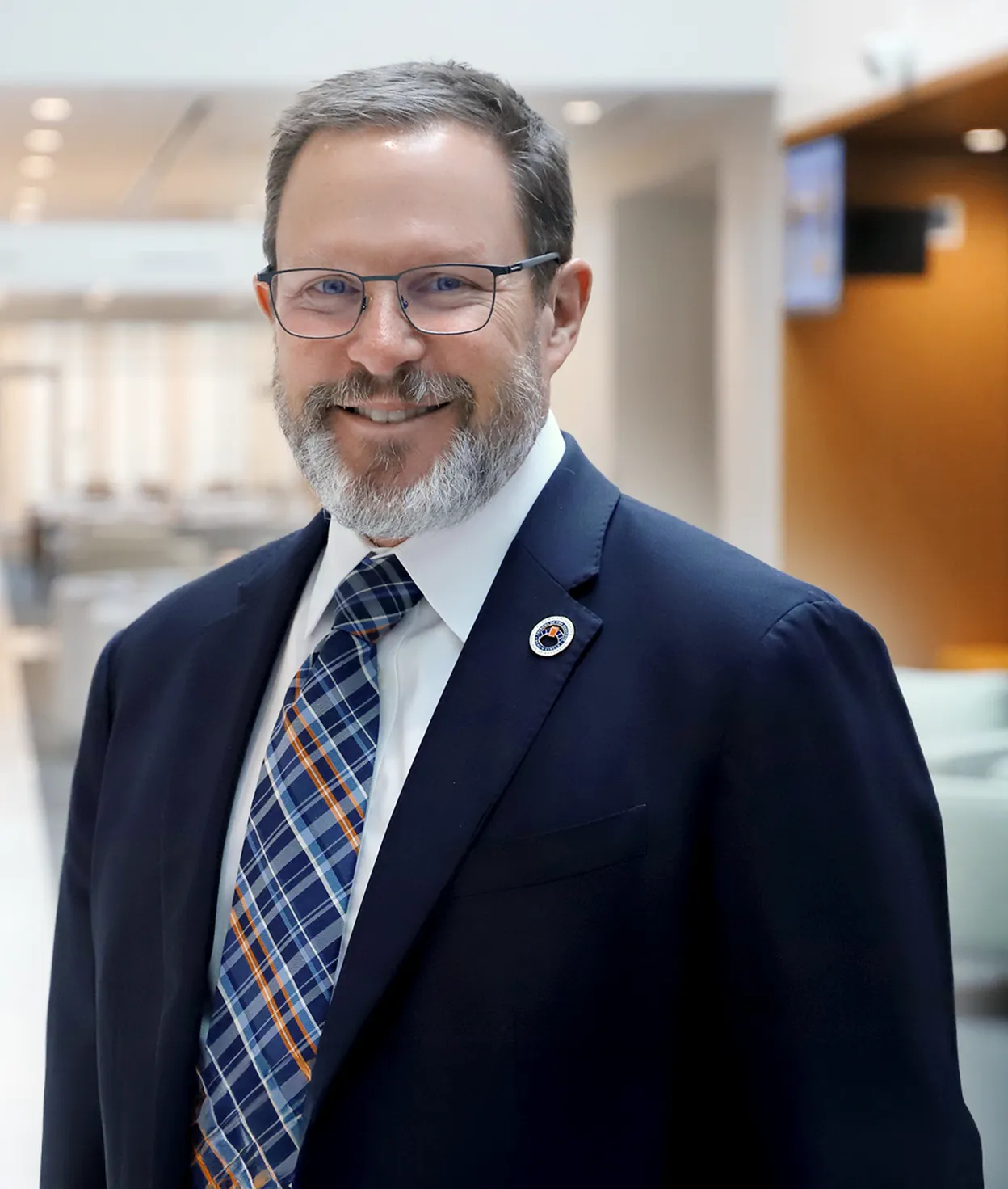 Portrait of Dean Fairbrother smiling in a suit and glasses in a bright Auburn University hallway.