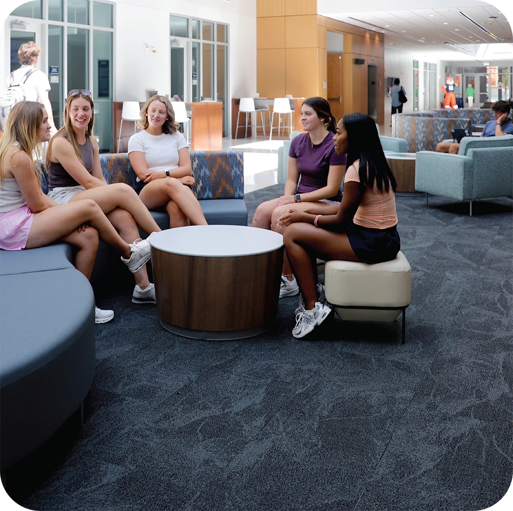 Five Auburn students sit together in a bright campus lounge, talking around a round table.