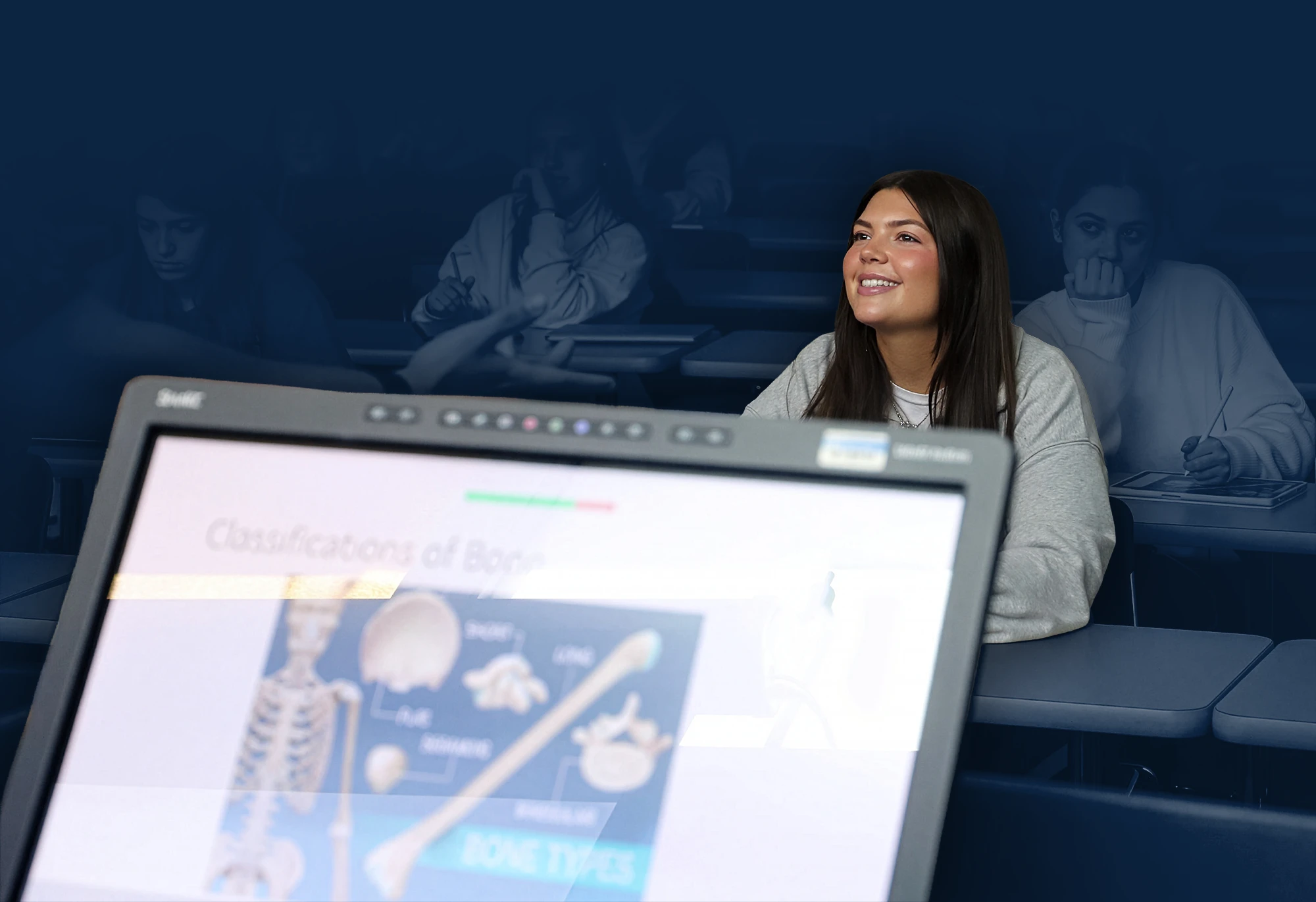 ella Helm sits in class smiling, with a tablet on the desk in front of her.